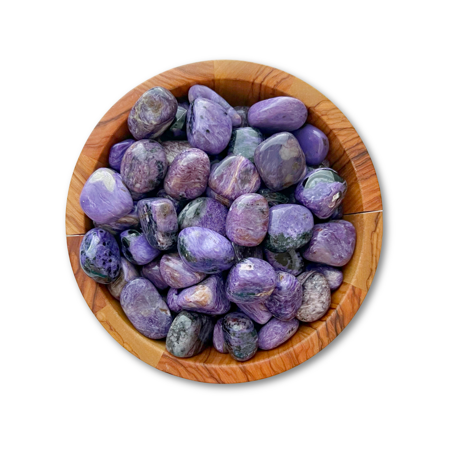 A wooden bowl filled with Charoite Tumbled Stones, displaying various shades of purple. The stones are smooth and glossy, each unique in its hue and pattern. The bowl’s natural wood grain adds a contrasting earthy touch to the vibrant gems, enhancing their spiritual insight properties.