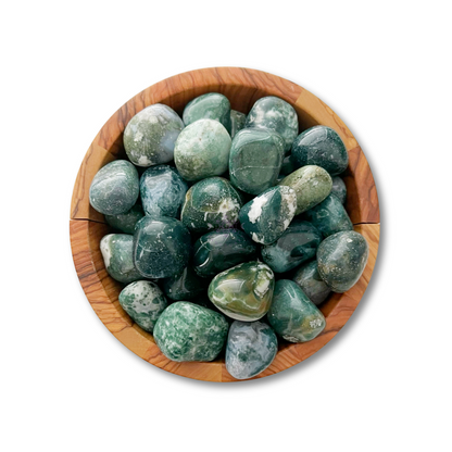 A round wooden bowl filled with polished Green Moss Agate Tumbled Stones of various shades, featuring smooth surfaces and slight color variations. The stones, known for their healing properties and symbolizing new beginnings, are neatly arranged within the bowl, which is set against a plain white background.