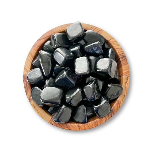 A wooden bowl filled with smooth, polished Shungite Tumbled Stones. The stones have a shiny surface, reflecting light in various spots. Known to balance the root chakra and shield against EMFs, the bowl provides a natural contrast to their sleekness. The image is taken from a top-down perspective against a white background.