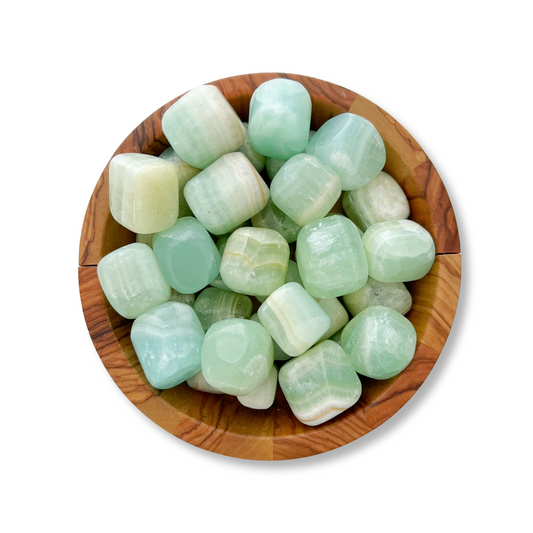 A wooden bowl contains numerous smooth, cube-shaped Pistachio Green Calcite Tumbled Stones with a polished, glossy finish in varied shades of green. Some stones exhibit white banding, reminiscent of pistachio green calcite. The bowl features a natural wood grain texture, evoking a sense of forgiveness and compassion.