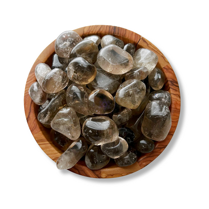 A wooden bowl filled with smooth, polished Smoky Quartz Tumbled Stones sits against a plain white background. The stones, known for their grounding stone qualities and healing properties, vary in shades of translucent gray and brown, with natural inclusions and cracks visible within them.