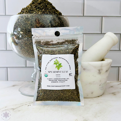 A package of Spearmint Leaf is displayed in front of a glass bowl filled with more dried spearmint and a white marble mortar and pestle. The label highlights metaphysical uses such as clarity, communication, joy, protection, purification, strength, and vitality for spell-casting endeavors.