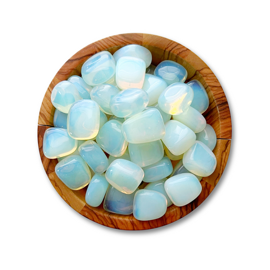 A wooden bowl filled with smooth, polished Opalite Tumbled Stones. The stones have a translucent, milky appearance with subtle hues of blue, green, and hints of yellow, each reflecting light in a soft, ethereal manner. Renowned for their healing properties, these meditation stones rest against a plain white background.