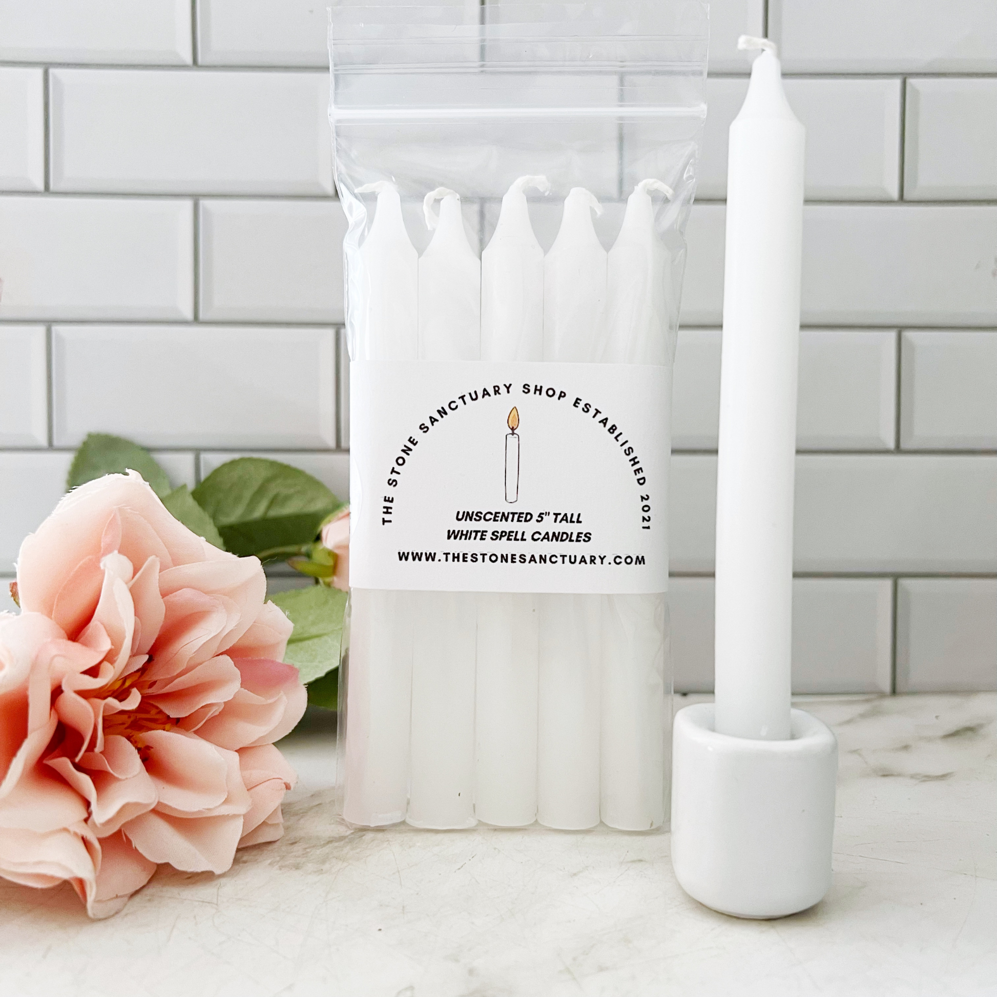 A bundle of six 5" White Chime Candles held together by a black string, placed on a light-colored wooden surface. The 5" White Chime Candles are unlit, with wicks visible at the top, perfect for spellwork.