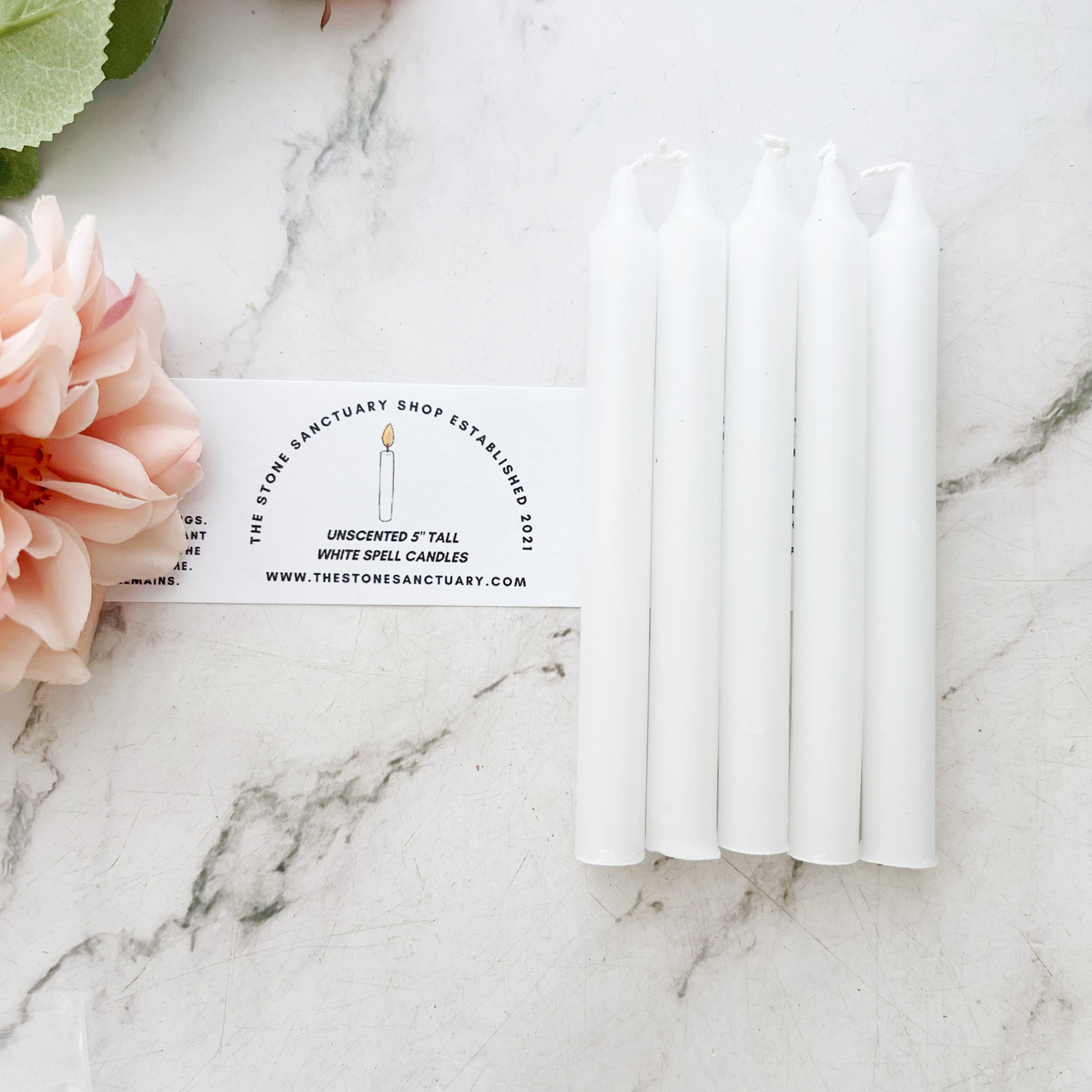 A bundle of six 5" White Chime Candles held together by a black string, placed on a light-colored wooden surface. The 5" White Chime Candles are unlit, with wicks visible at the top, perfect for spellwork.