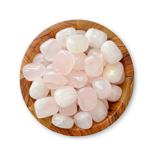 A wooden bowl filled with polished, translucent, pale pink Pink Calcite Tumbled Stones emanates an aura of emotional healing. The smooth, rounded stones have a glossy finish that catches the light to reveal their soft, milky appearance. The bowl sits on a plain white background.