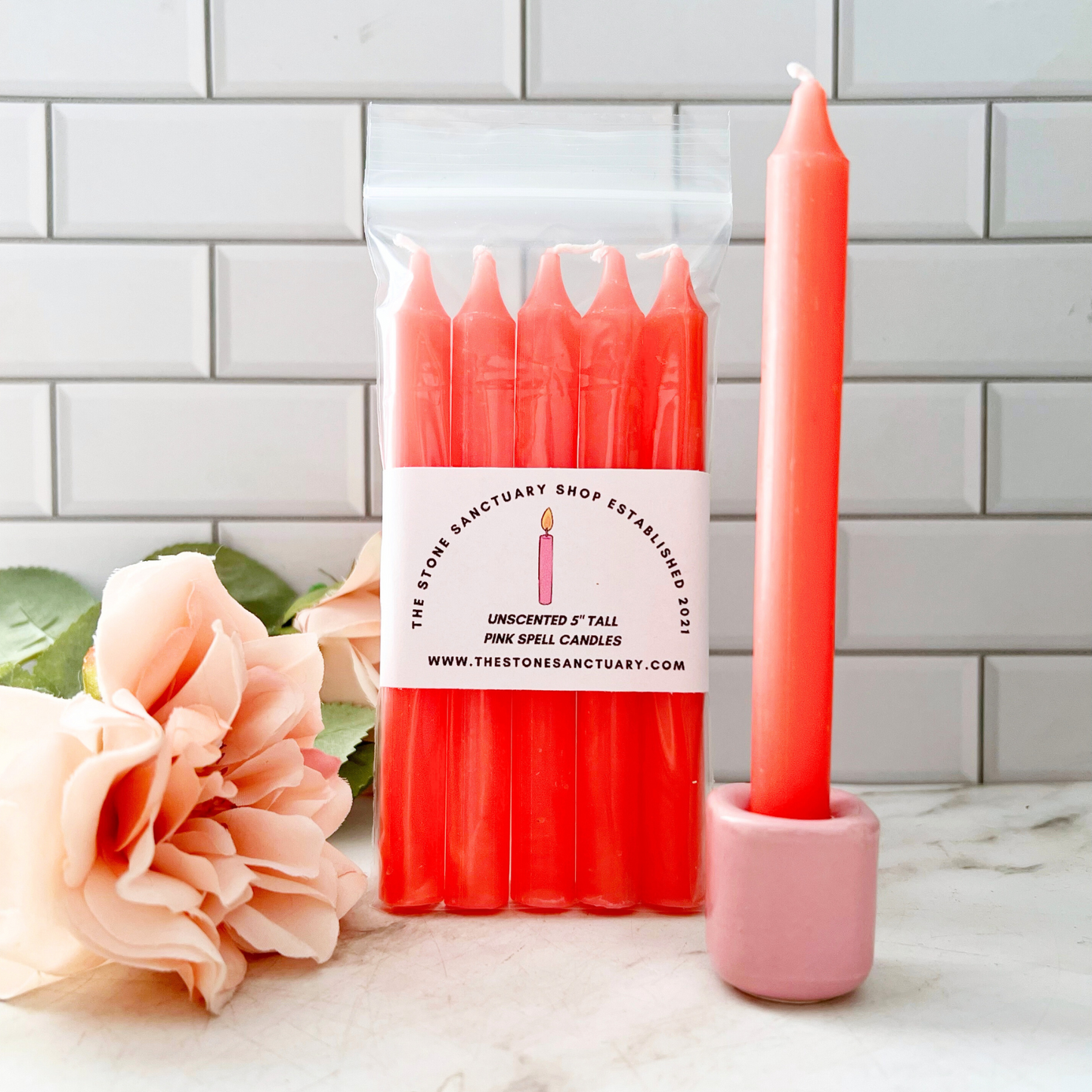 A bundle of four 5" Pink Chime Candles, tied together with a black string, placed on a white wooden surface. These ritual candles are evenly aligned, showing their pointed tips clearly against the light background.