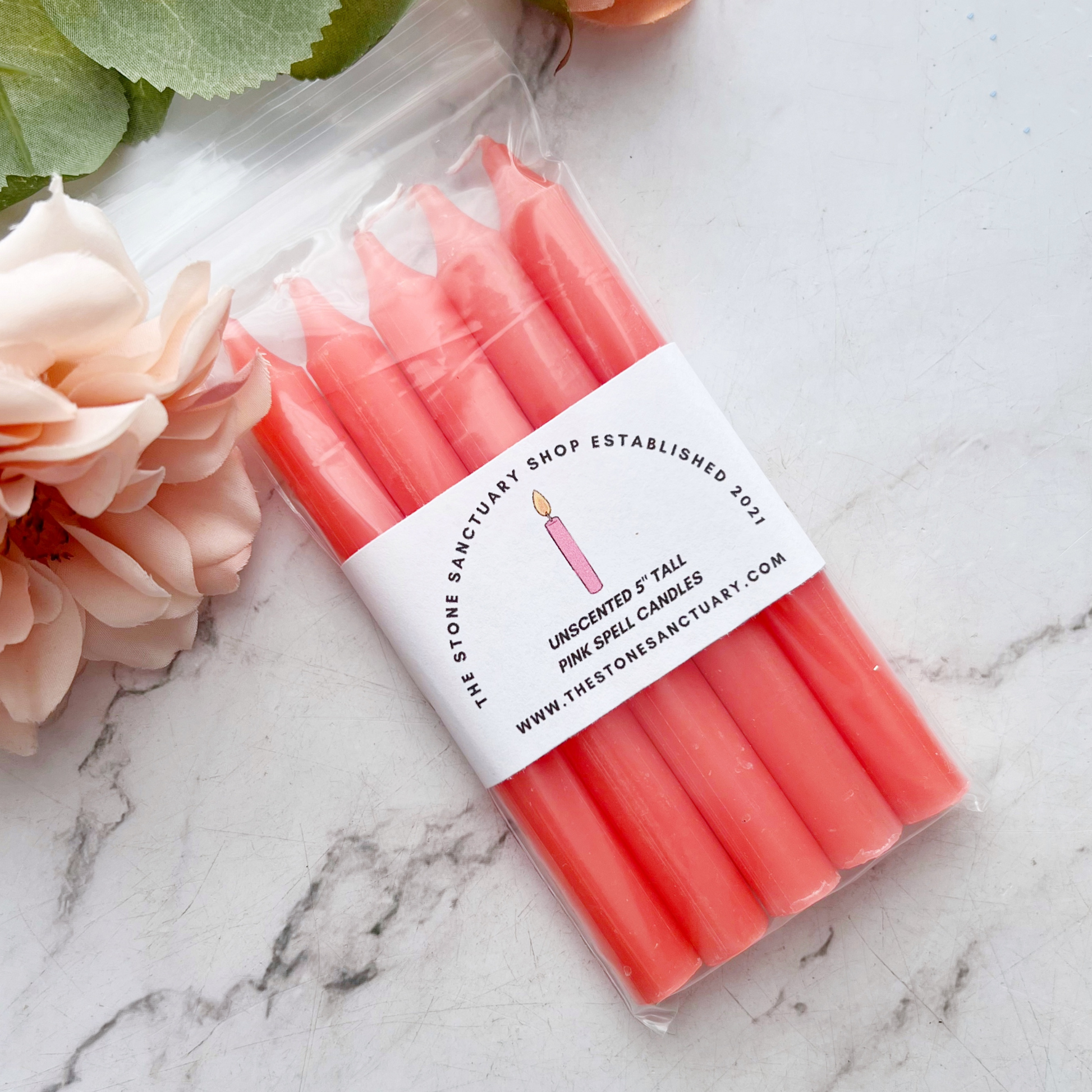 A bundle of four 5" Pink Chime Candles, tied together with a black string, placed on a white wooden surface. These ritual candles are evenly aligned, showing their pointed tips clearly against the light background.