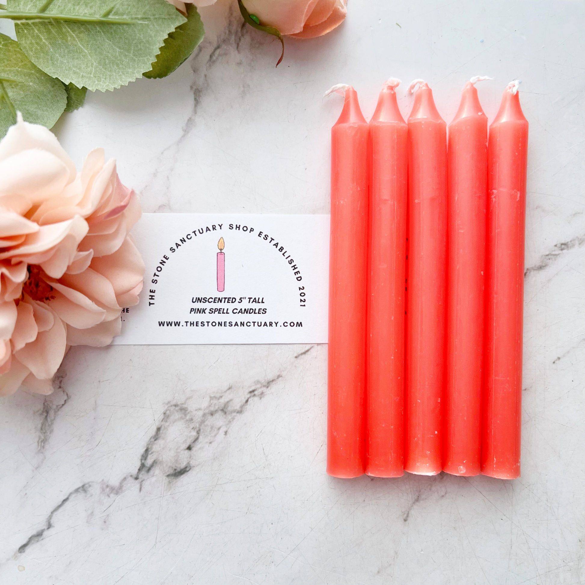 A bundle of four 5" Pink Chime Candles, tied together with a black string, placed on a white wooden surface. These ritual candles are evenly aligned, showing their pointed tips clearly against the light background.