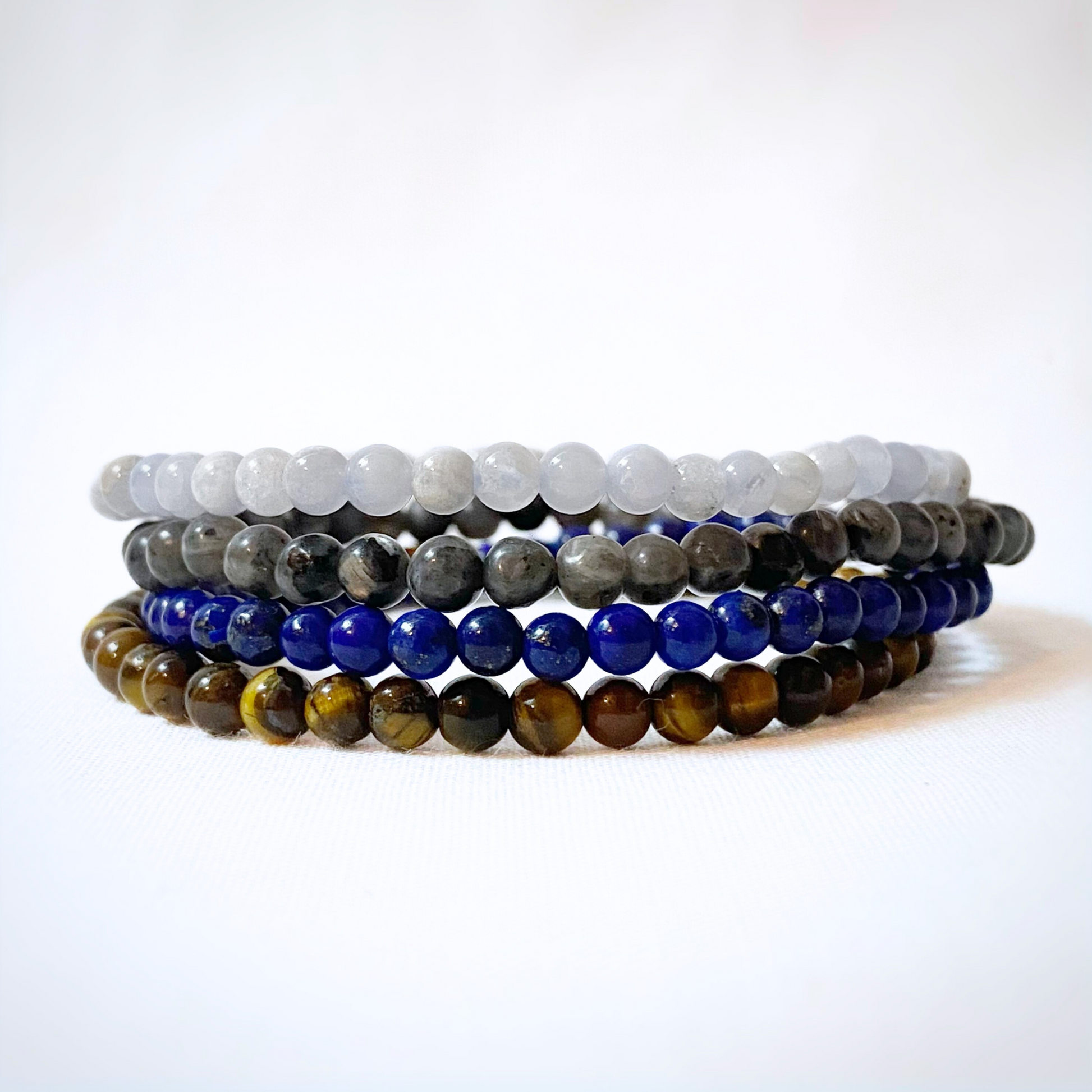 An image of a Gemini Bracelet Set featuring stacks of gemstone bracelets in blue, brown, and gray tones. Text describes traits of Gemini (gentle, adaptable, curious) and promotes Reiki-infused energy bracelets made of Blue Lace Agate, Labradorite, Lapis Lazuli, and Tiger Eye.