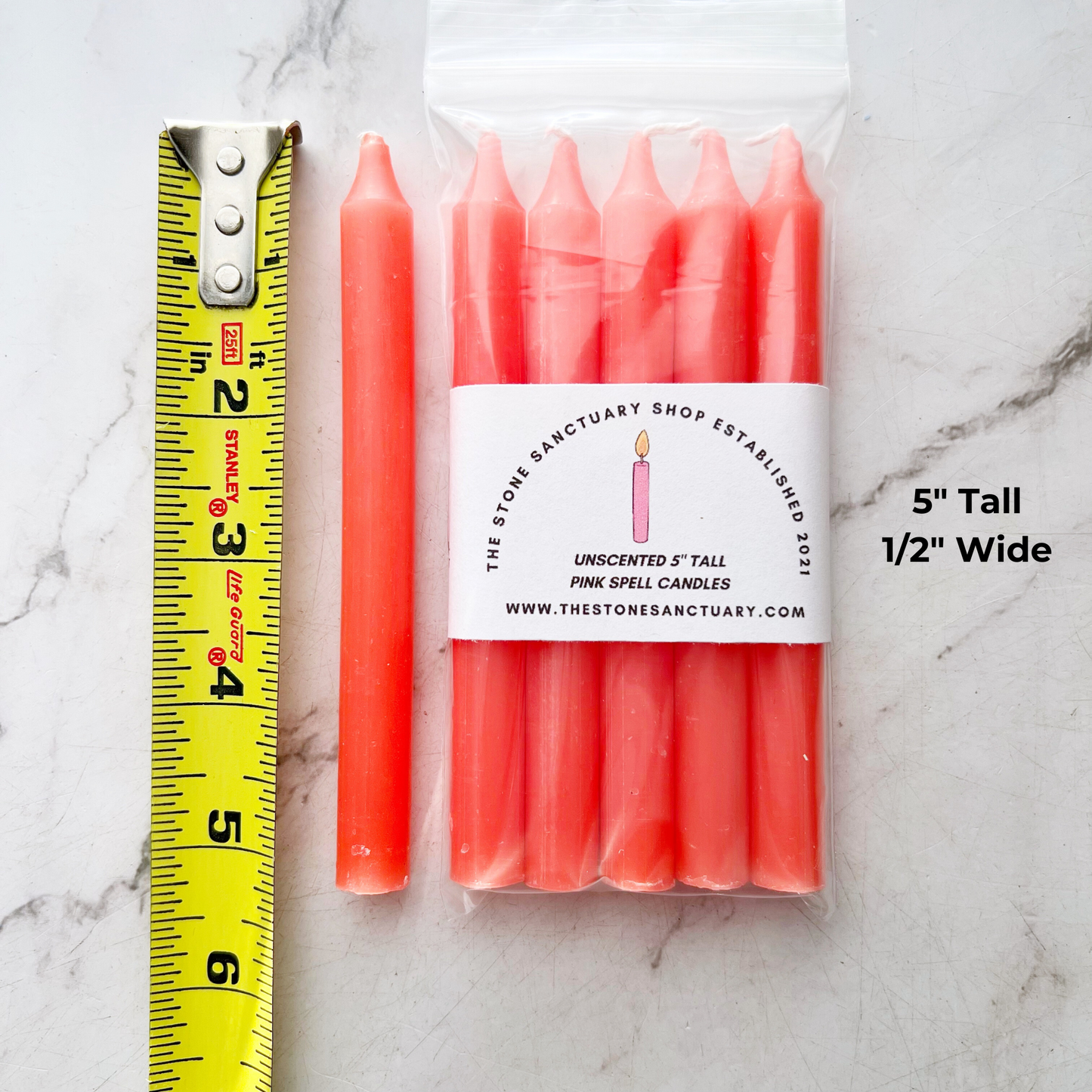 A bundle of four 5" Pink Chime Candles, tied together with a black string, placed on a white wooden surface. These ritual candles are evenly aligned, showing their pointed tips clearly against the light background.