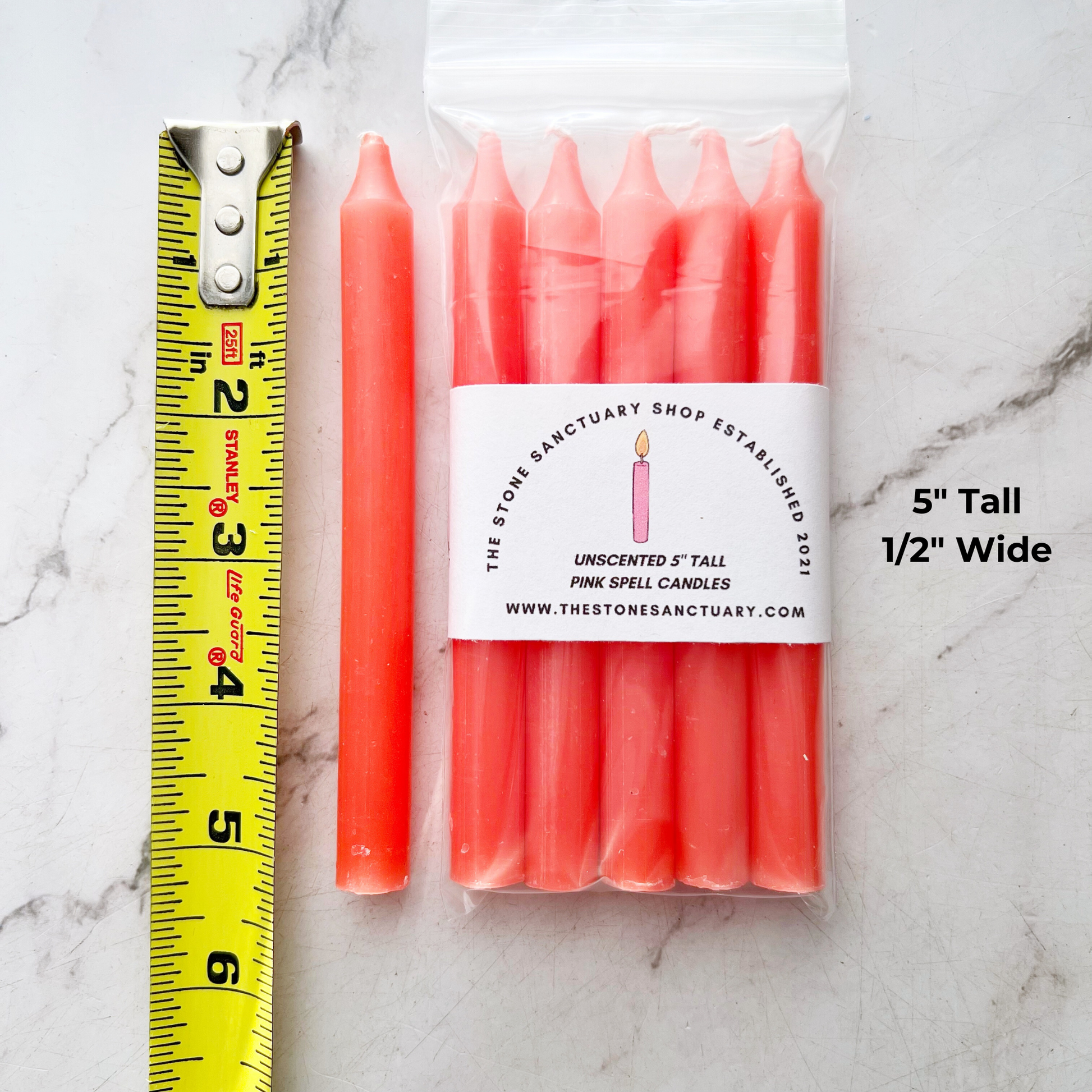 A bundle of four 5" Pink Chime Candles, tied together with a black string, placed on a white wooden surface. These ritual candles are evenly aligned, showing their pointed tips clearly against the light background.