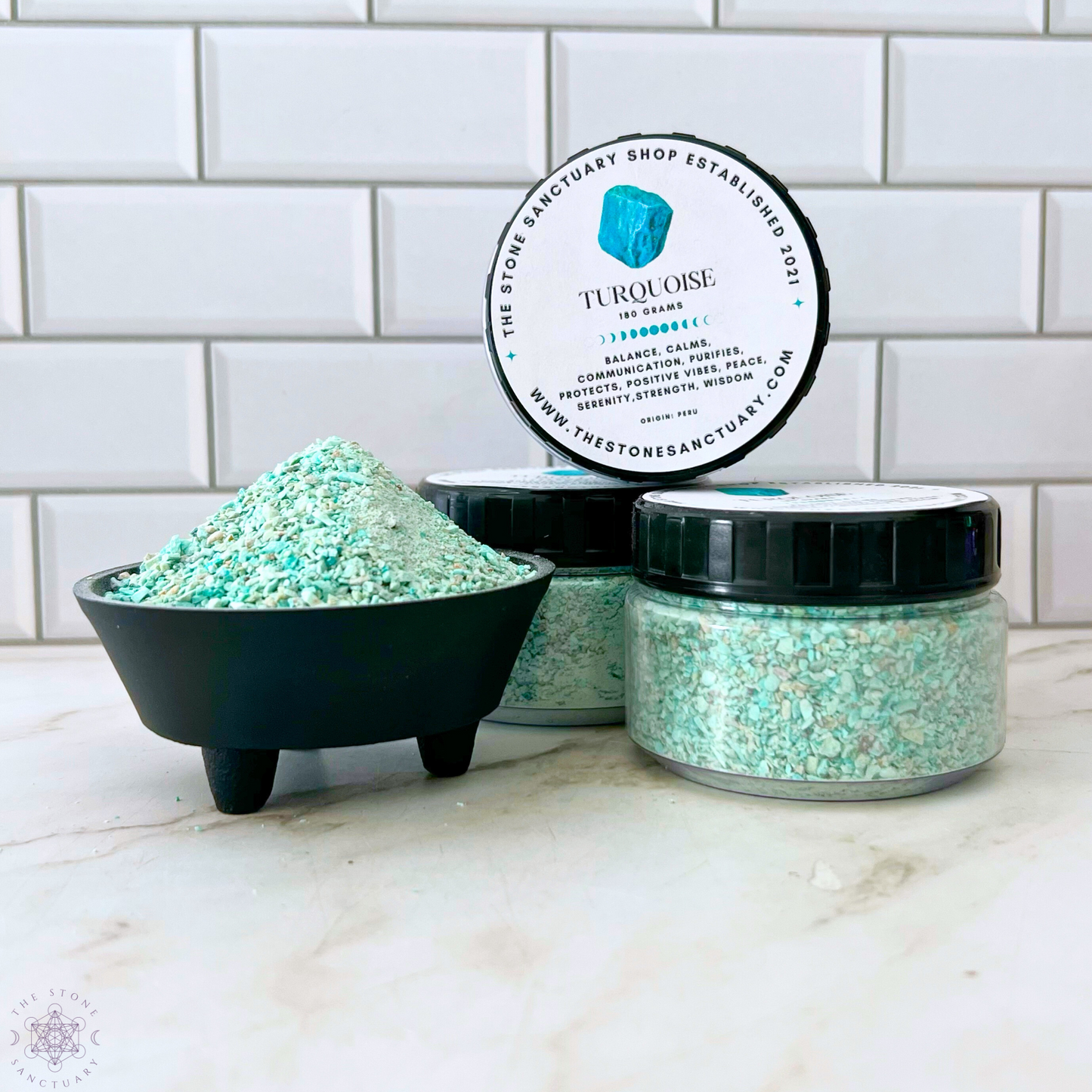 Three containers of turquoise-colored bath salts are displayed against a white tiled background. One container is open, showing a small pile of Peruvian Turquoise Gemstone Sand inside, while another is sealed. The third container has its lid standing upright, featuring product details.