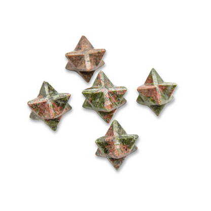 Five small, intricately carved Mini Unakite Merkaba star-shaped stones with a blend of green and pink colors are scattered on a white background. The stones have a textured, marbled appearance that promotes emotional balance.