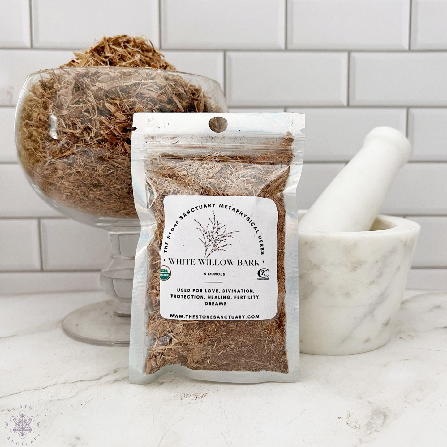 **A sealed package of dried White Willow Bark rests on a white surface in front of a mortar and pestle. Behind the package is a glass bowl filled with more White Willow Bark. The setting features white subway tile in the background, perfect for those interested in spiritual rituals or metaphysical uses.**