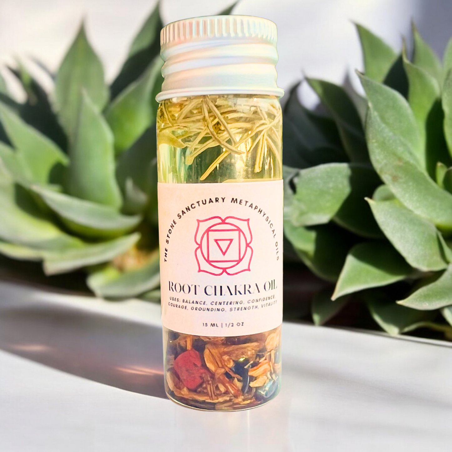 A petite clear bottle, labeled "Root Chakra Oil," is filled with dried herbs and delicate flowers. Featuring a white cap, the bottle is set against a backdrop of lush green foliage, crafting a natural and serene scene that inspires feelings of grounding and stability.