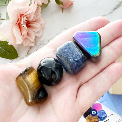 An image titled "Crystals for Evil Eye Protection" featuring Onyx, Rainbow Hematite, Tiger Eye, and Lapis Lazuli crystals. Each healing crystal is described with its protective properties. In the center is an image of an evil eye symbol, emphasizing their role in a comprehensive **Evil Eye Crystal Kit**.