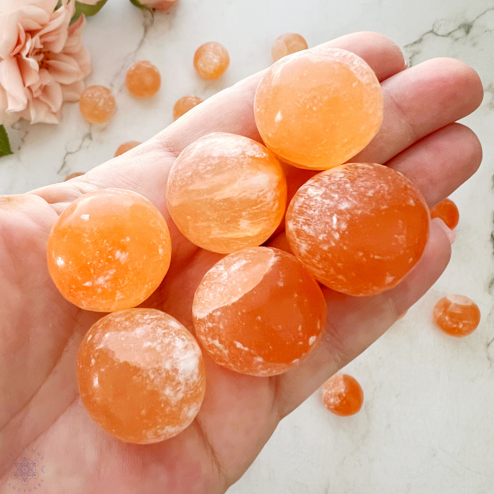 A top view of a wooden bowl filled with numerous round, orange candies resembling Orange Selenite Tumbled Sphere Stones. The candies have a slightly translucent appearance, with a sugary coating visible on their surfaces, invoking thoughts of emotional well-being. The bowl is set against a white background.