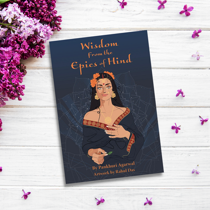 The product titled "Wisdom from the Epics of Hind" by Pankhuri Agarwal with artwork by Rahul Das is placed on a white wooden surface surrounded by purple and white flowers. This self-help tool draws from Hindu epics, featuring a cover illustration of a woman in traditional attire with orange flowers in her hair.