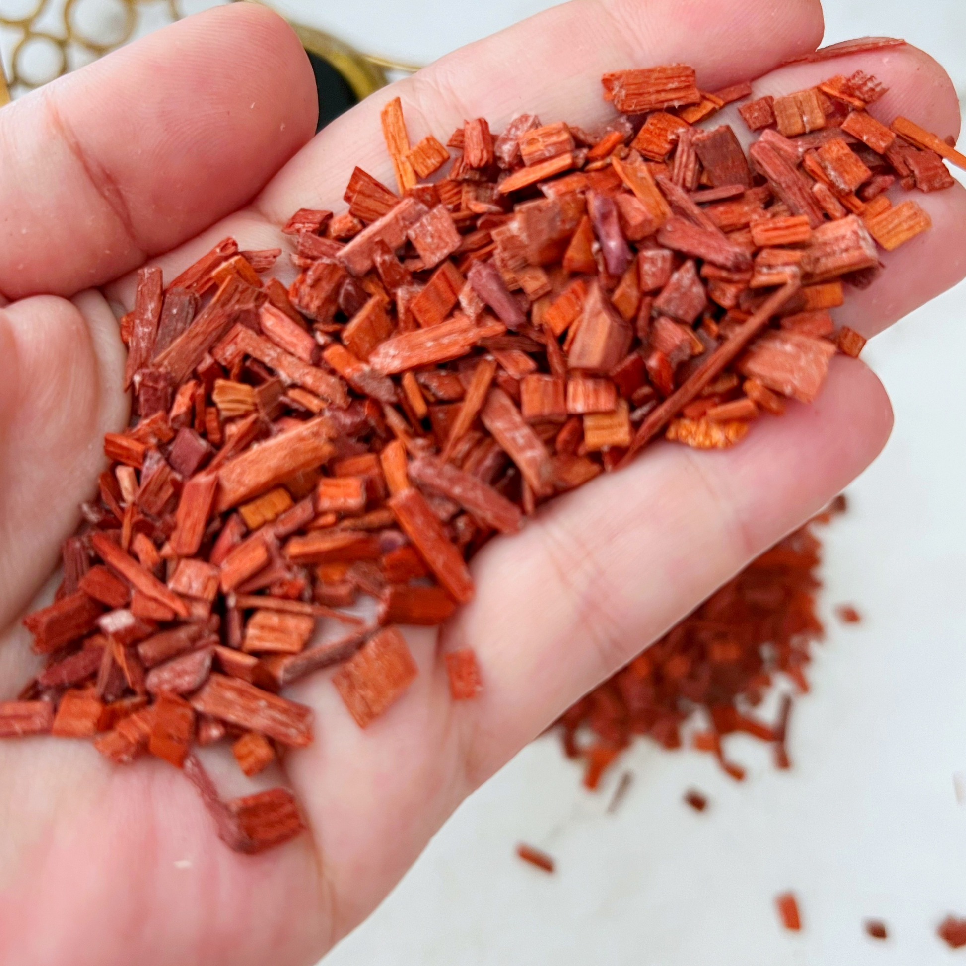 A wooden bowl filled with Red Sandalwood Chips is placed on a white surface. The background features a dark blue wall and golden decorative crescent moon and star elements. Text at the bottom of the image reads "RED SANDALWOOD.