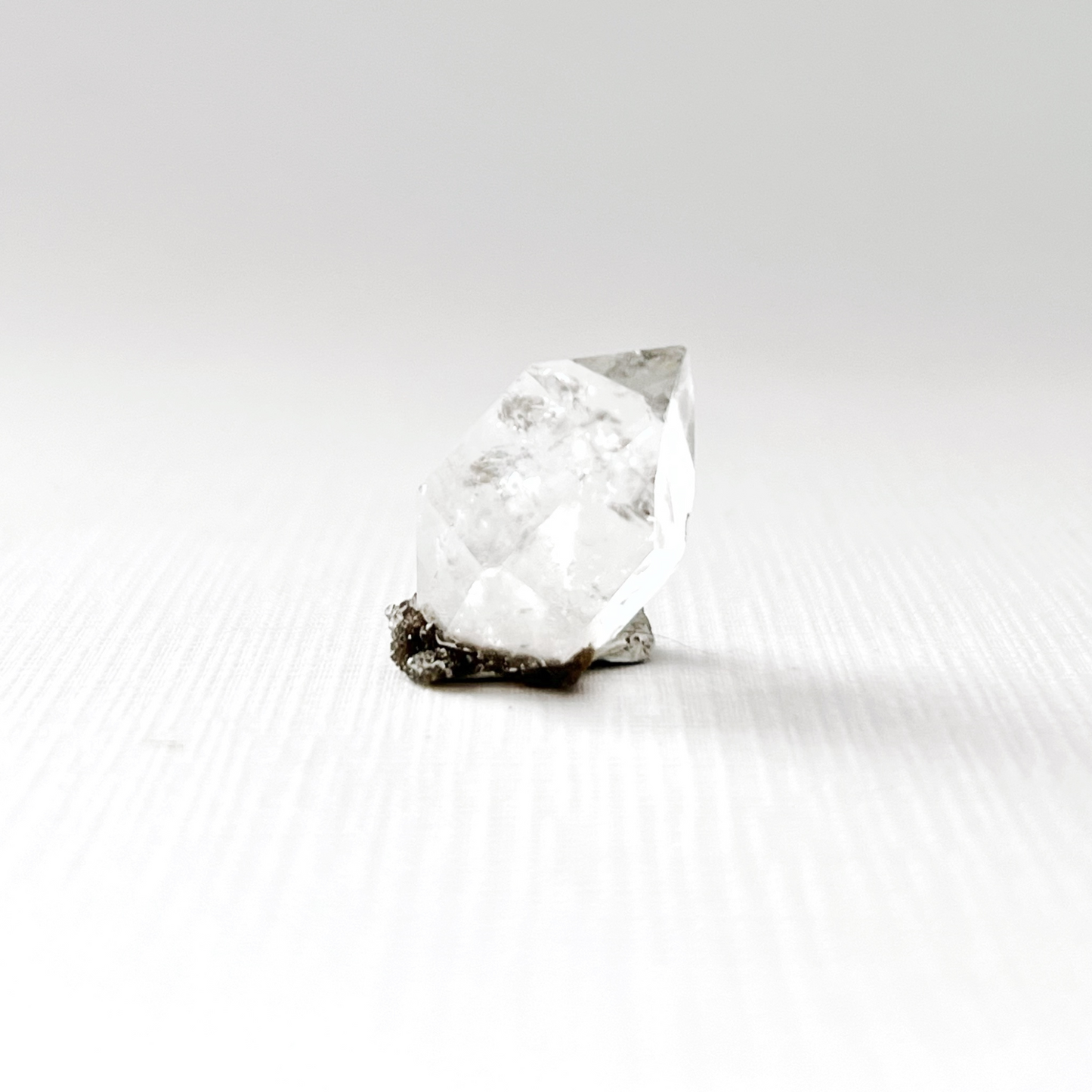 A single, .68" Raw Herkimer Diamond is shown against a black background. The unique, powerful crystal's reflective surface creates a mirrored image on the dark surface beneath it, highlighting its sharp edges and intricate internal structure.