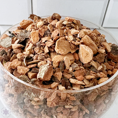 A small, holographic bag of Birch Bark, labeled "Birch Bark - Betula pubescens," is displayed in front of a larger glass bowl filled with birch bark pieces. A white marble mortar and pestle sit beside the bag. The background features a white tiled wall, highlighting its potential metaphysical uses.