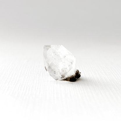 A single, .68" Raw Herkimer Diamond is shown against a black background. The unique, powerful crystal's reflective surface creates a mirrored image on the dark surface beneath it, highlighting its sharp edges and intricate internal structure.