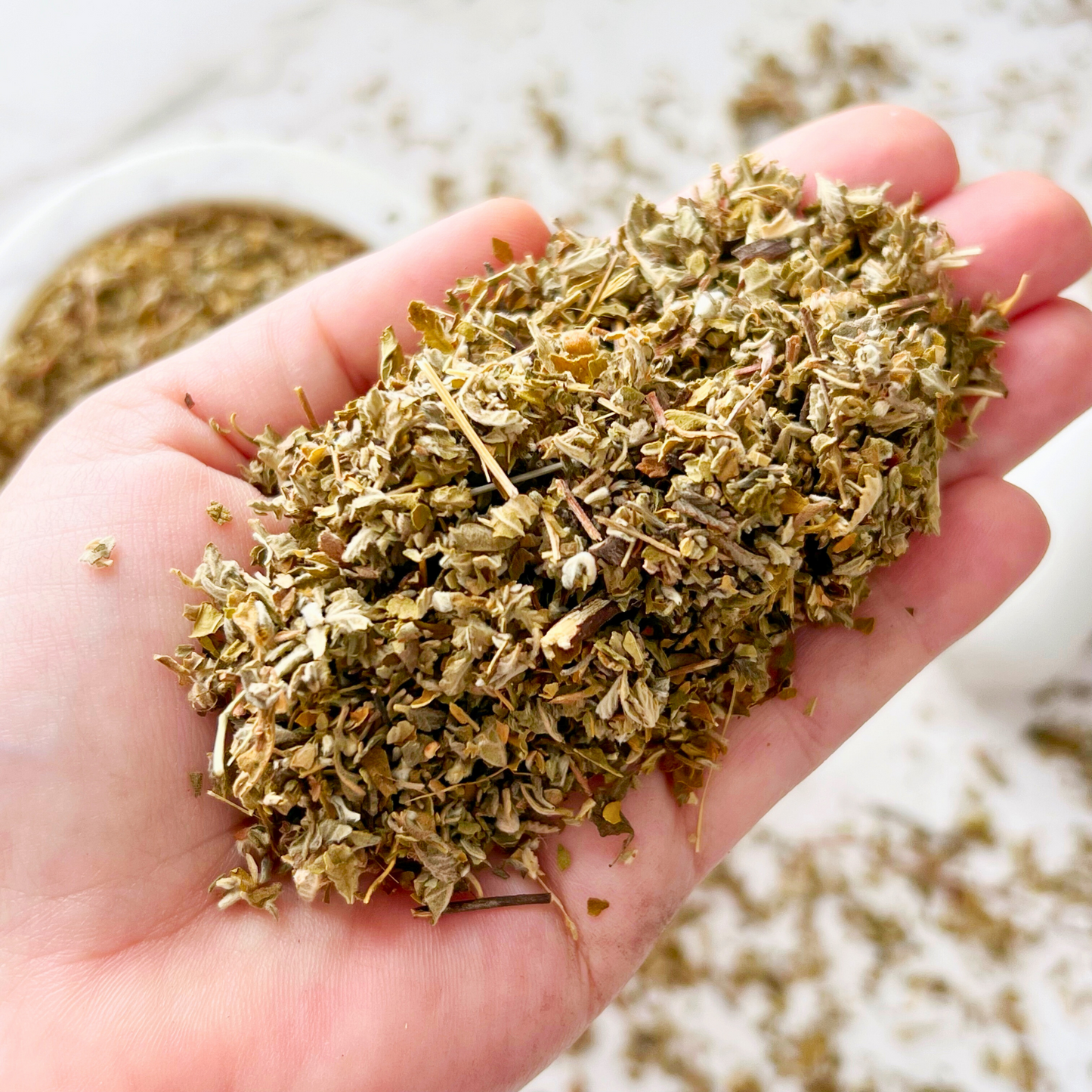 A bag labeled "Damiana Leaf" is placed in front of a glass bowl filled with Damiana Leaf. To the right, a white mortar and pestle are visible. This setup is against a white tiled background, suggesting uses such as enhancing dreams, work, love, energy, and other metaphysical practices.