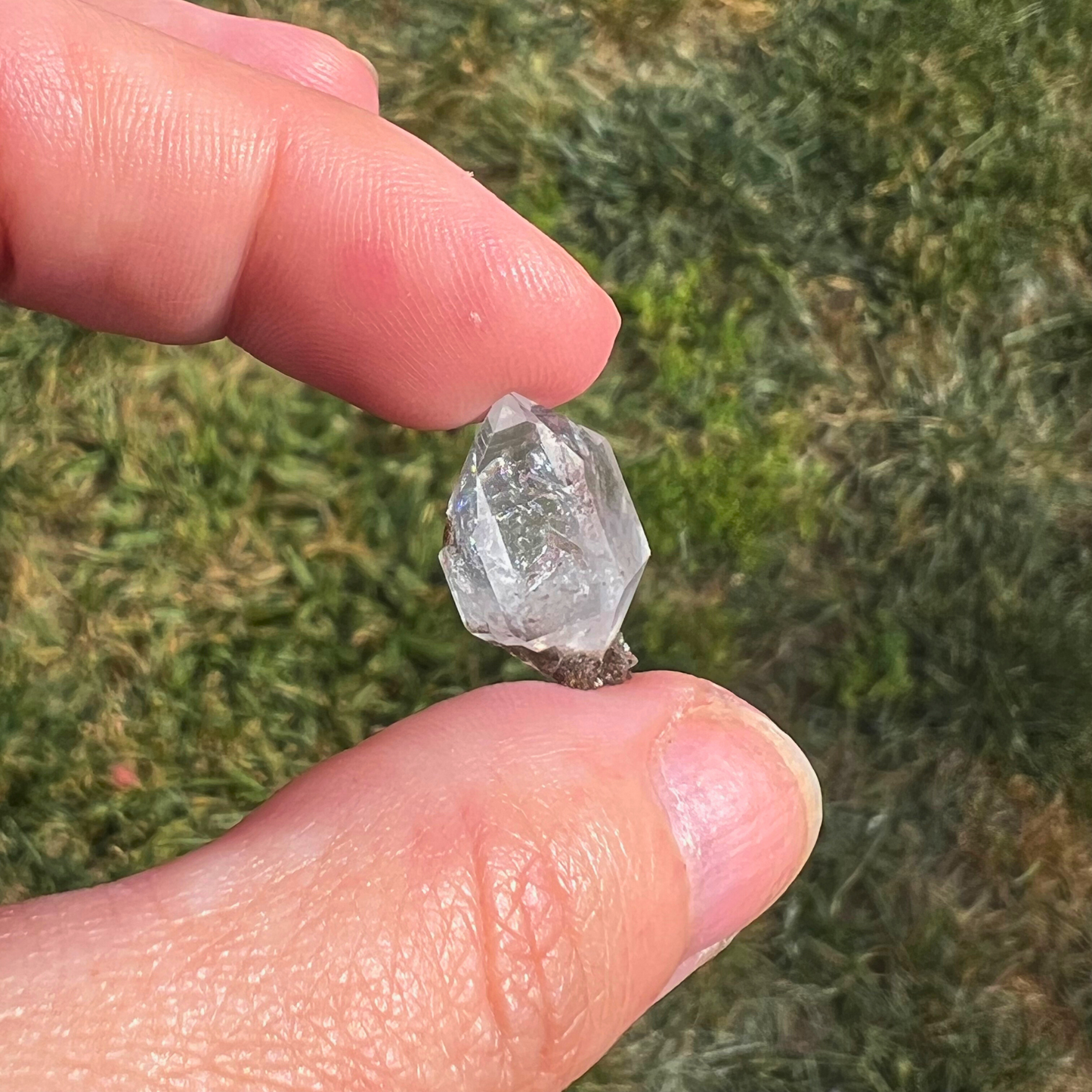 A single, .68" Raw Herkimer Diamond is shown against a black background. The unique, powerful crystal's reflective surface creates a mirrored image on the dark surface beneath it, highlighting its sharp edges and intricate internal structure.