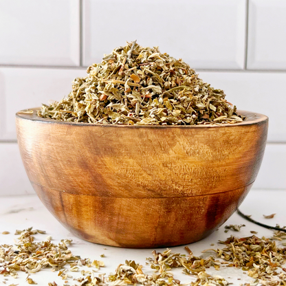 A bag labeled "Damiana Leaf" is placed in front of a glass bowl filled with Damiana Leaf. To the right, a white mortar and pestle are visible. This setup is against a white tiled background, suggesting uses such as enhancing dreams, work, love, energy, and other metaphysical practices.