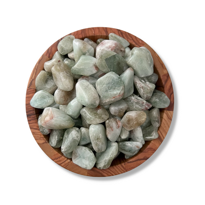 A wooden bowl filled with smooth, polished Prasiolite Tumbled Stones sits against a white background. The stones vary in shades of green and have slight touches of white and brown markings, perfect for balancing the Heart Chakra.