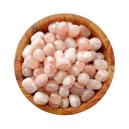 A wooden bowl filled with Strawberry Pink Calcite Tumbled Stones, known for their heart chakra benefits. The stones are smooth and rounded, displaying various shades of pink. The bowl's natural wood grain adds contrast to the soft hues of the Strawberry Pink Calcite, enhancing its emotional healing properties against a plain white background.