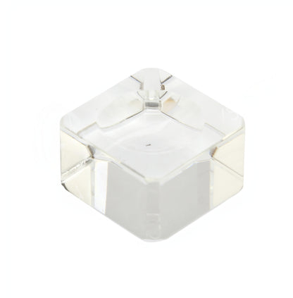 A small, transparent 1" Clear Glass Cube Sphere Holder, perfect for a gemstone sphere display, is pictured against a plain white background. The cube features smooth, clear surfaces and sharp edges, with a slight reflection on its faces indicating its glossy texture.