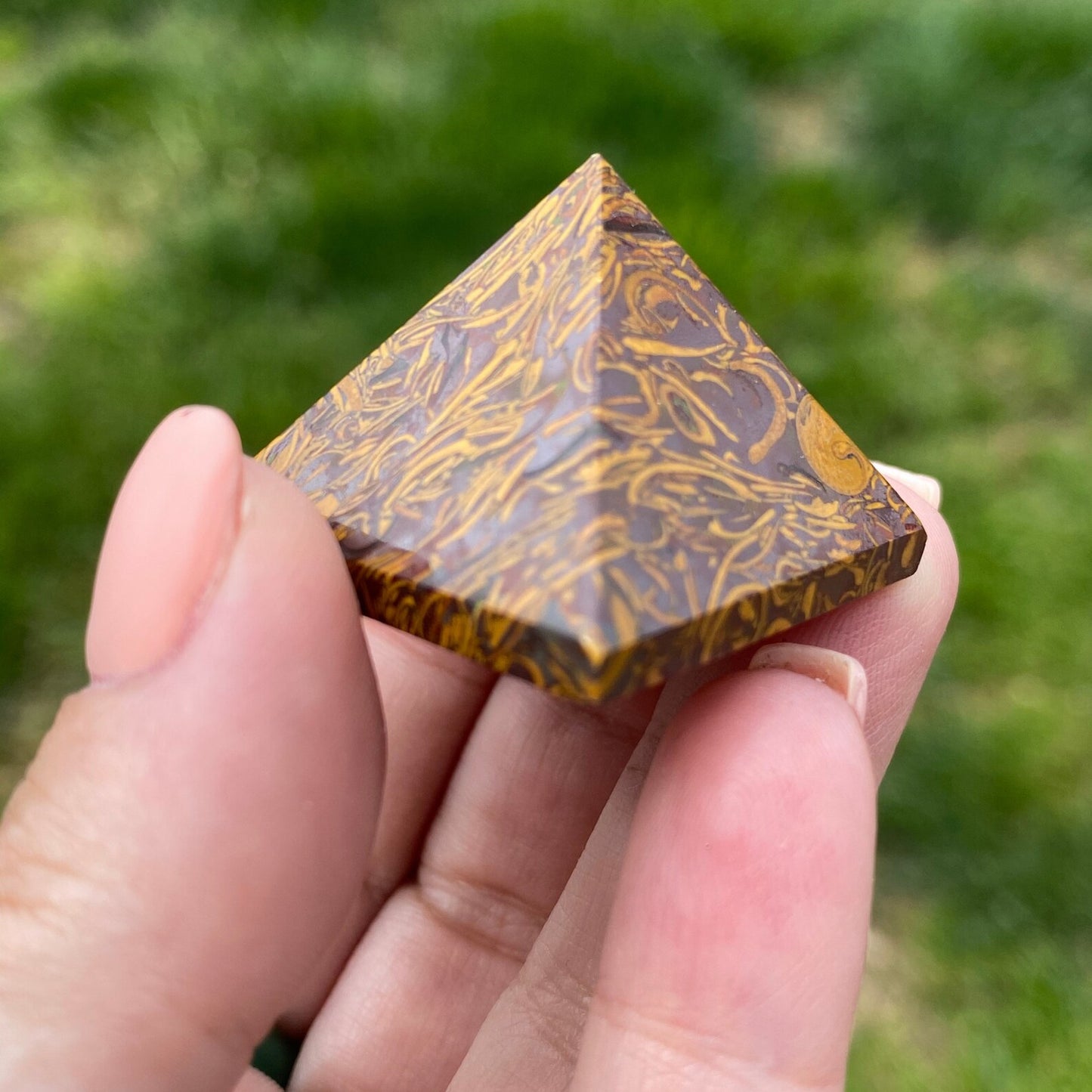 Three small, brown 1" Mini Calligraphy Jasper Pyramids with intricate patterns sit on a white surface in front of a white brick wall. Behind the pyramids, there is a bundle of sage tied with white string, resting on a wooden tray.