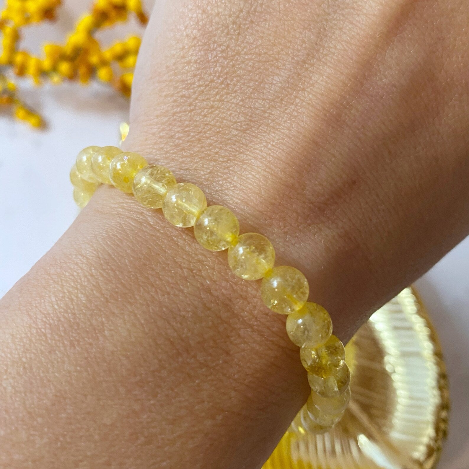 A 6mm Citrine Beaded Bracelet is displayed against a black background. The polished beads have a translucent quality and reflect light, giving the bracelet a radiant appearance. Known for its Usui Reiki energy, this manifestation stone adds a touch of magic to your wrist.