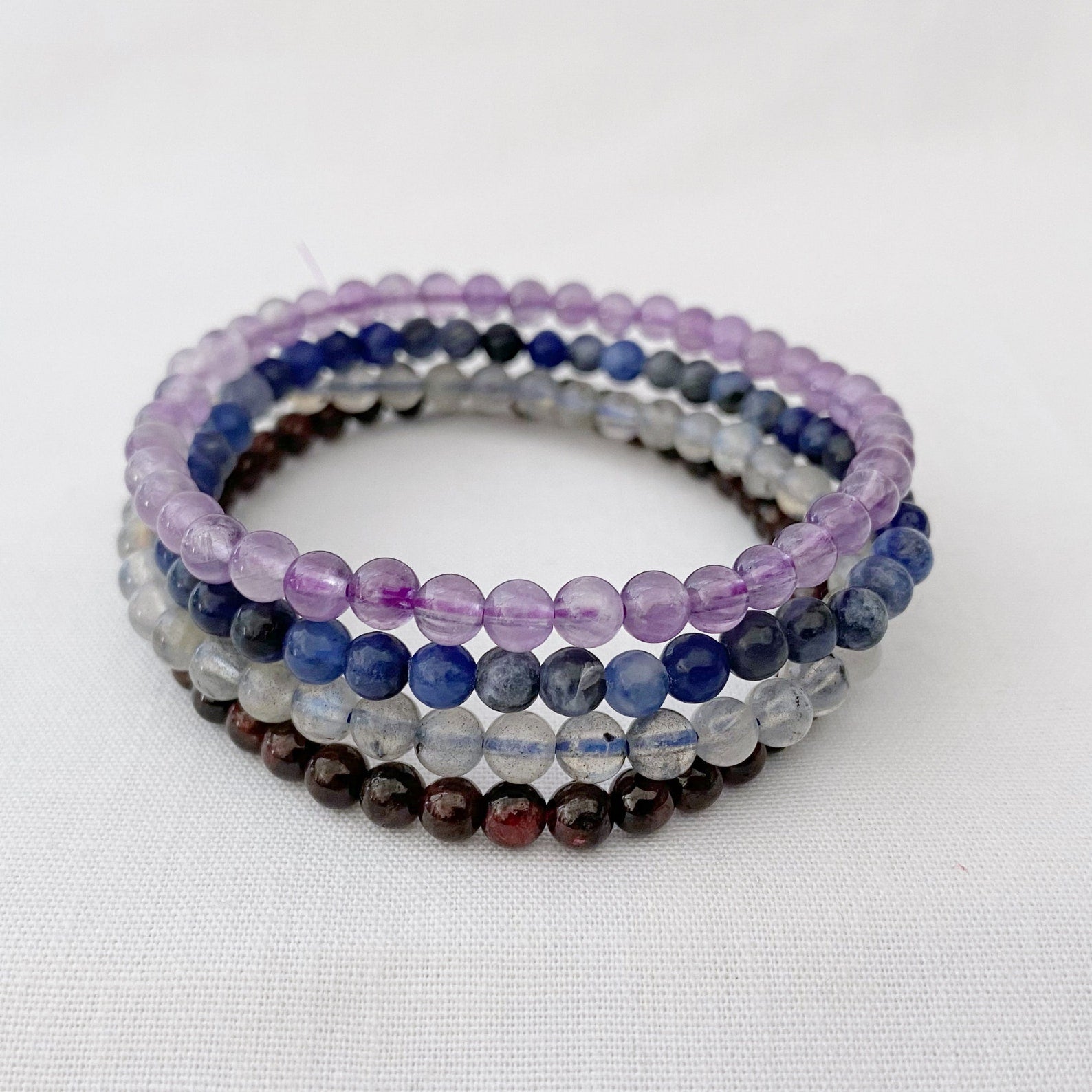 The image showcases an "Aquarius Beaded Bracelet Set" with four beaded bracelets stacked vertically. Highlighting the positive traits of Aquarius (January 20 - February 18), it features stones like Labradorite, Amethyst, Sodalite, and Garnet in each Aquarius Beaded Bracelet.