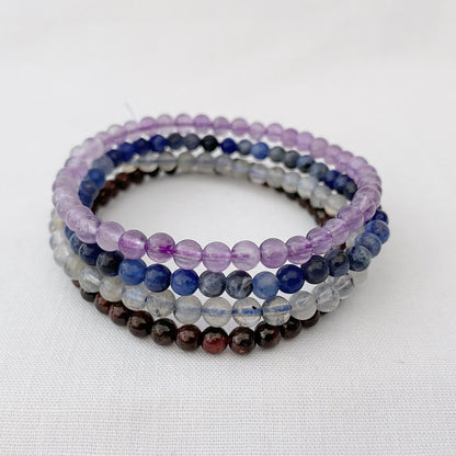 The image showcases an "Aquarius Beaded Bracelet Set" with four beaded bracelets stacked vertically. Highlighting the positive traits of Aquarius (January 20 - February 18), it features stones like Labradorite, Amethyst, Sodalite, and Garnet in each Aquarius Beaded Bracelet.