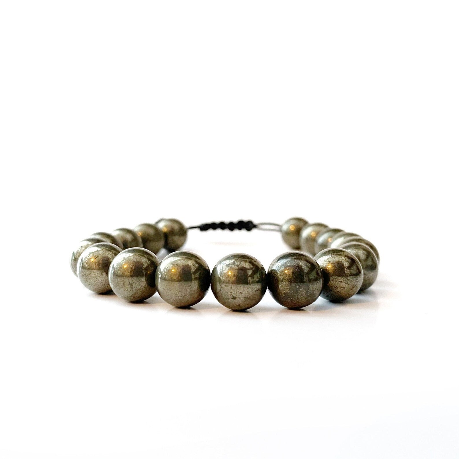 A fashionable accessory, the 10mm Pyrite Beaded Bracelet showcases metallic, polished, spherical pyrite beads elegantly arranged in a circular shape. The reflections on the beads highlight their smooth and shiny surface, set against a plain white background.