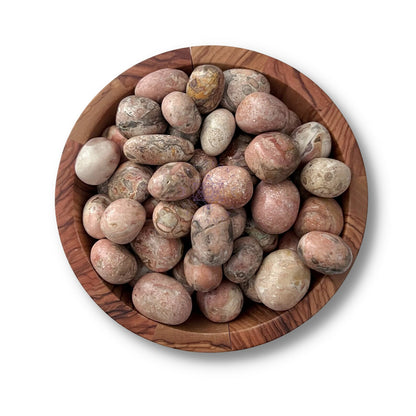 A wooden bowl filled with polished Pink Picasso Jasper Tumbled Stone on a white background. The stones, in shades of pink and gray, have various patterns that create a visually appealing mix of colors and textures, perfect for adding grounding energies and emotional balance to your space.