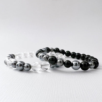 Two **8mm Terahertz Beaded Bracelets** are displayed on a white surface. The bracelet on the left features alternating Clear Quartz and silver beads, while the bracelet on the right consists of alternating Black Tourmaline and silver beads. Both bracelets have a minimalist and elegant design.