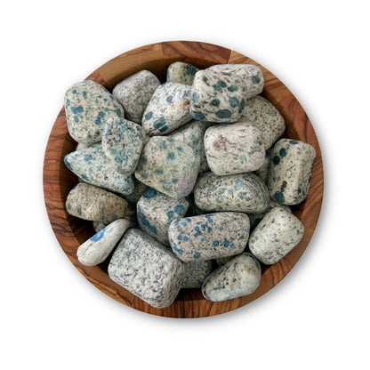 A round wooden bowl filled with white and blue speckled, irregularly shaped K2 Jasper Tumbled Stones. The tumbled crystals vary in size and have a smooth texture, creating a visually interesting contrast against the natural wood grain of the bowl. The background is plain white.