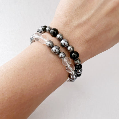 Two **8mm Terahertz Beaded Bracelets** are displayed on a white surface. The bracelet on the left features alternating Clear Quartz and silver beads, while the bracelet on the right consists of alternating Black Tourmaline and silver beads. Both bracelets have a minimalist and elegant design.