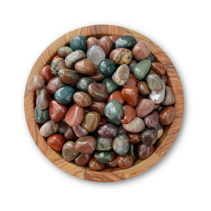 A wooden bowl filled with an assortment of polished, multicolored stones. Among them, you'll find Fancy Jasper Tumbled Stones in shades of red, green, brown, and gray, creating a visually appealing collection. The background is white.