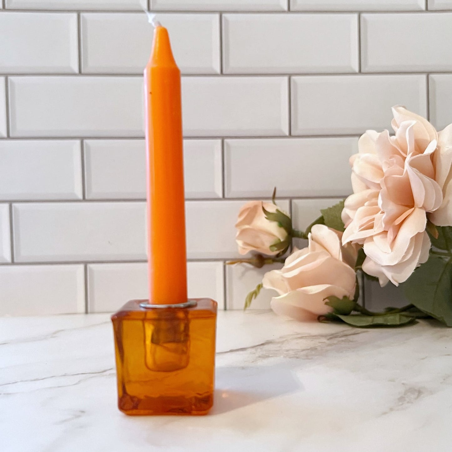 A set of eight colorful candles, each in a 1" Mini Glass Cube Holder for Ritual Candles of matching color, arranged in a line on a white tiled surface. Colors from left to right are: deep purple, dark blue, teal, light blue, green, yellow, orange, and red.