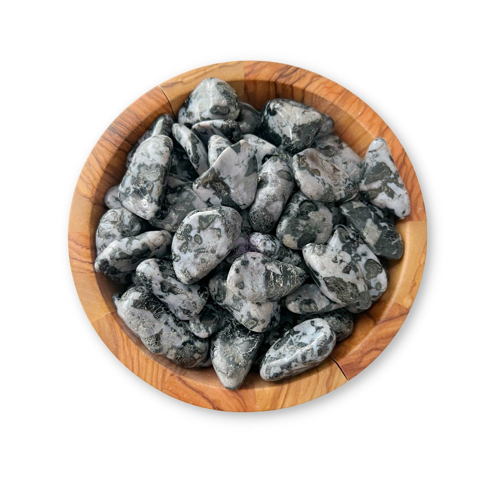 A wooden bowl filled with polished Indigo Gabbro Tumbled Stones, alongside a few dazzling Mystic Merlinite pieces. The stones are mostly gray with intricate black and white tree-like patterns. The bowl has a rich, natural wood grain, set against a white background.