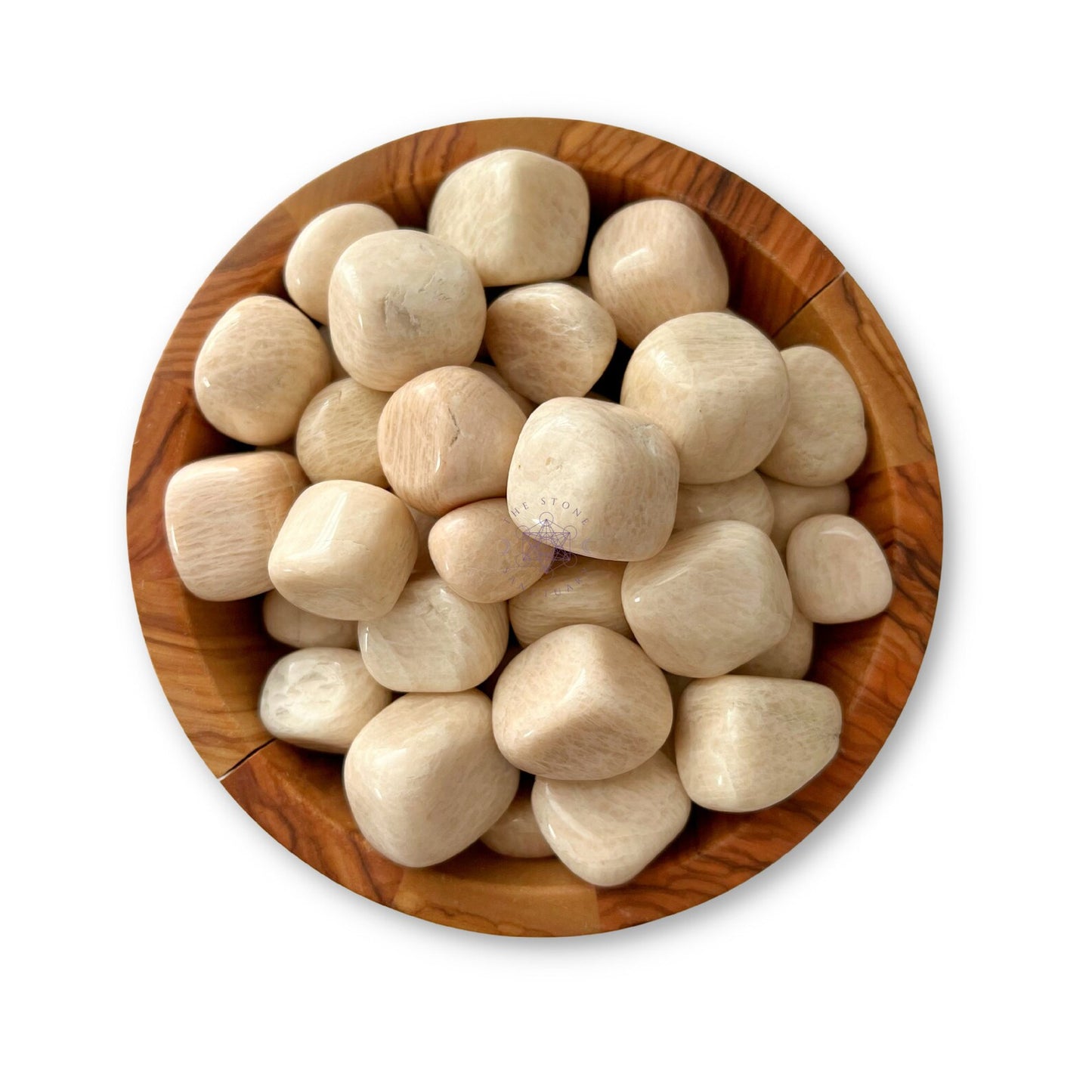 A wooden bowl filled with polished, light-colored Peach Moonstone Tumbled Stones. The stones are smooth and rounded, appearing to be of similar size and shape, and they contrast with the natural grain and tone of the wooden bowl. The bowl is set against a white background.