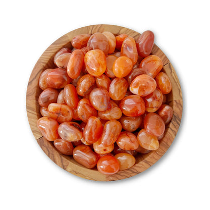 A round wooden bowl filled with polished, oval-shaped Carnelian Tumbled Stones in varying shades of orange, red, and brown. The stones have a glossy finish and are arranged closely together, showcasing their natural patterns and hues. These fertility crystals enhance motivation. The bowl is set against a white background.