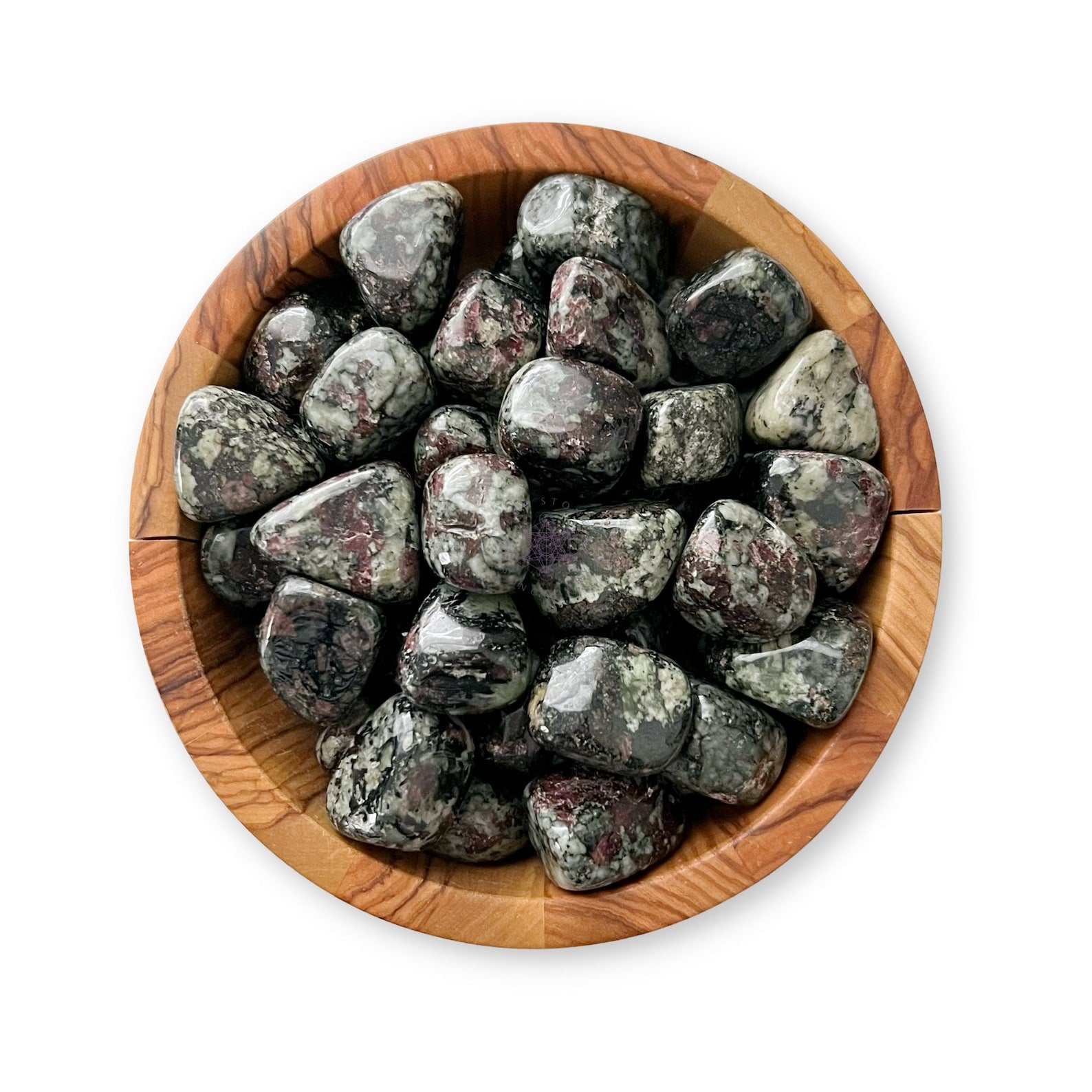 A wooden bowl filled with polished, smooth stones featuring a mix of dark and light streaks and patches in various shades of gray, black, and maroon. This exquisite crystal collection includes Eudialyte Tumbled Stones. The bowl sits against a white background.