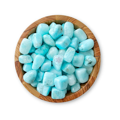 A wooden bowl filled with smooth, polished Blue Aragonite Tumbled Stones rests on a white background. The stones, ideal for balancing chakras during meditation, have a light turquoise hue with subtle white veining and variations in shade, giving them a calming and serene appearance.