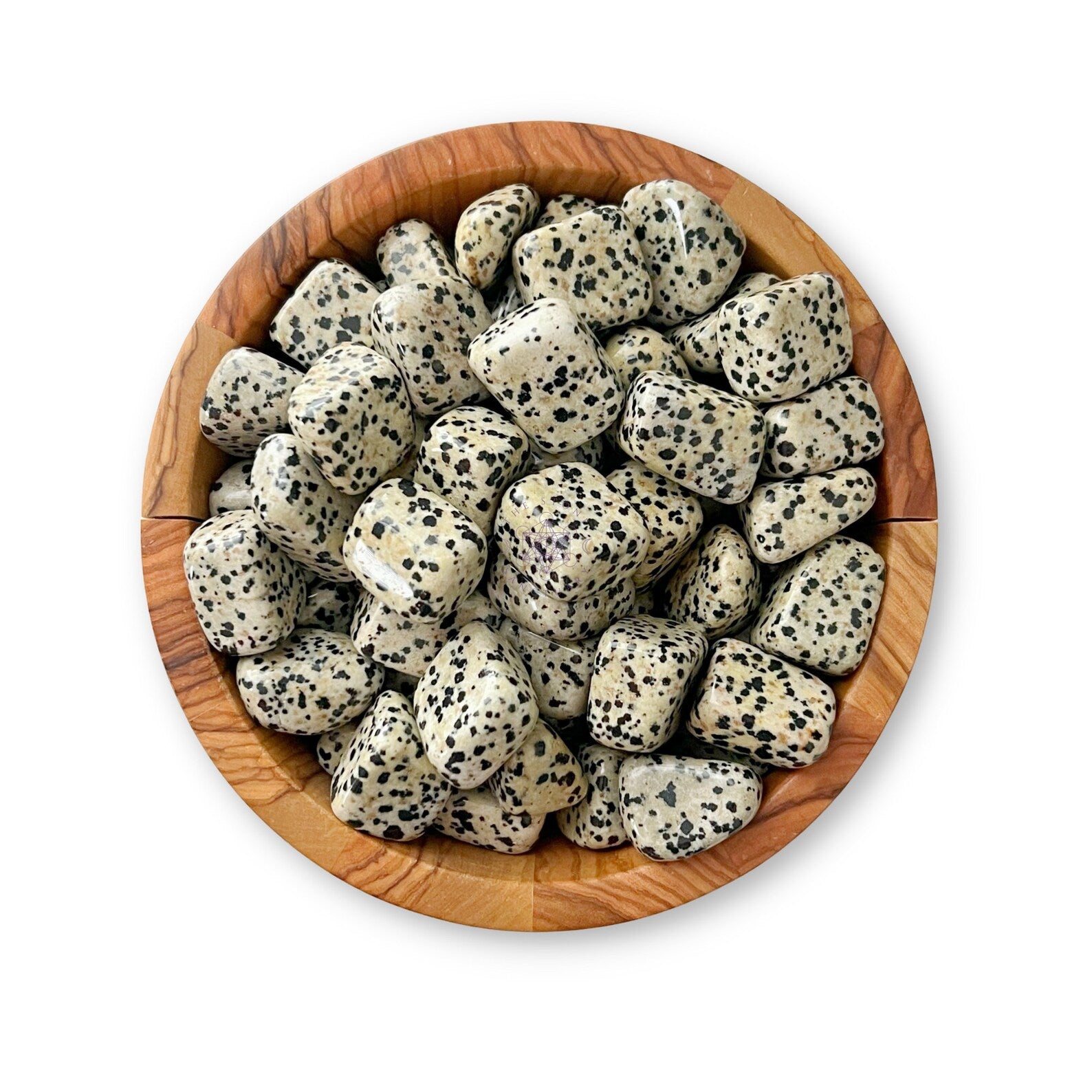 A wooden bowl filled with polished Dalmatian Jasper Tumbled Stones sits on a white background. The stones, light gray with black speckles, resemble the coat pattern of a Dalmatian dog and are known as a calming crystal for overthinkers.